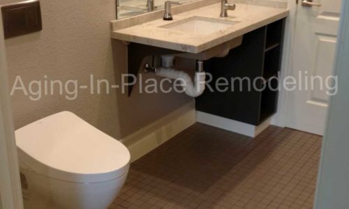 tile barrier free shower with built in shower seat for wheelchair accessibility, bathroom includes a wall mounted toilet and roll under sink