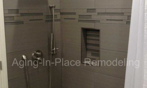 Wheelchair accessible tile shower in newly remodeled bathroom with ceiling lift, walk-in tub, wheelchair accessible sink and wall mounted toilet.