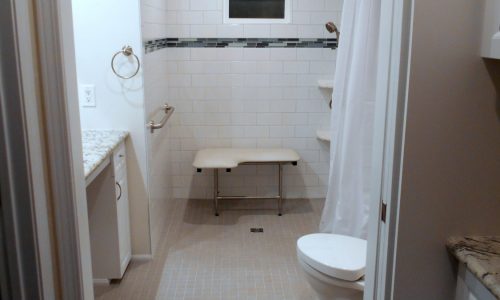 Wheelchair Accessible bathroom remodel with barrier free roll in shower, fold up shower seat, grab bars, hand held shower head, wheelchair accessible roll under sink