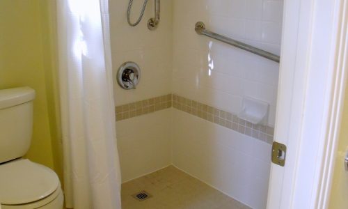 Tile roll-in, wheelchair accessible shower with teak fold up shower seat and grab bars for added safety