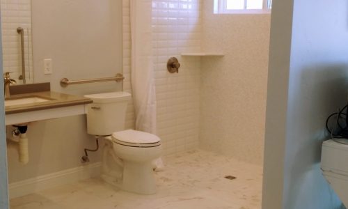 A wheelchair accessible bathroom remodel with roll-in tile shower, with roll under sink, hand held shower head and built in shower bench