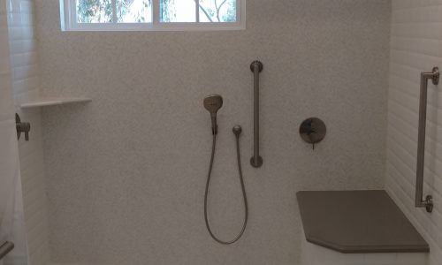 A wheelchair accessible bathroom remodel with roll-in tile shower, with roll under sink, hand held shower head and built in shower bench