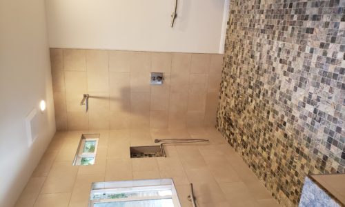 A wheelchair accessible bathroom including a custom tile barrier free shower, curved designer grab bars, built-in shower bench, roll under sink, hand held shower head and bidet toilet
