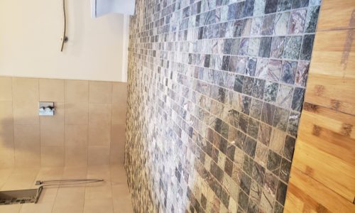 A wheelchair accessible bathroom including a custom tile barrier free shower, curved designer grab bars, built-in shower bench, roll under sink, hand held shower head and bidet toilet
