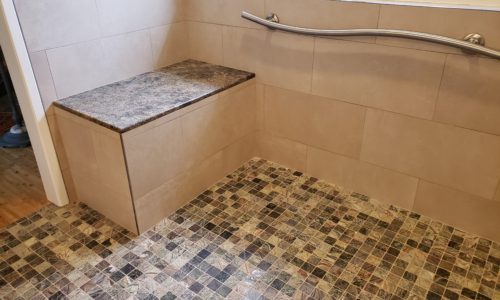 A wheelchair accessible bathroom including a custom tile barrier free shower, curved designer grab bars, built-in shower bench, roll under sink, hand held shower head and bidet toilet