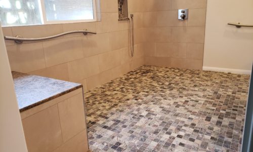 A wheelchair accessible bathroom including a custom tile barrier free shower, curved designer grab bars, built-in shower bench, roll under sink, hand held shower head and bidet toilet